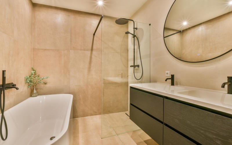 a modern bathroom with beige tiles on the walls, and a large round mirror over the bathtub in the corner